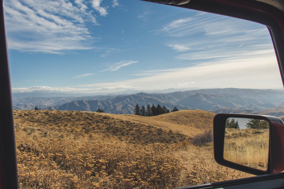 Breathtaking view of mountains and fields through a car window during a sunny autumn day.