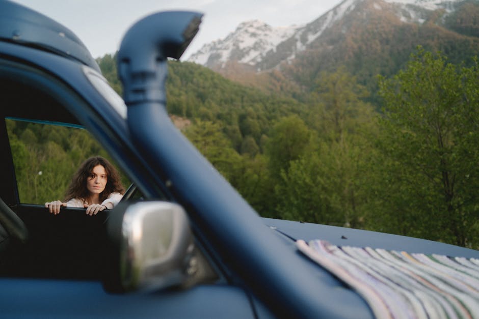 A woman leans out of a car window enjoying a mountain landscape.